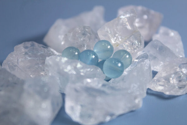 Polished aquamarine beads resting on rough clear quartz chunks against a soft blue background