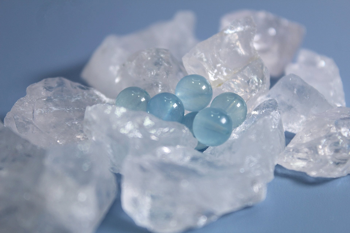 Polished aquamarine beads resting on rough clear quartz chunks against a soft blue background
