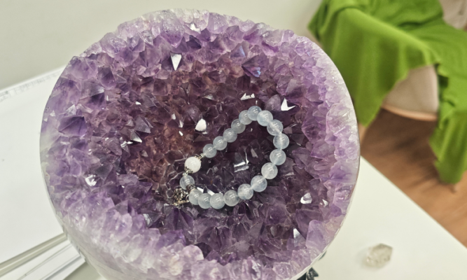 Blue rutilated quartz bracelet resting inside a large amethyst geode cluster for cleansing and recharging