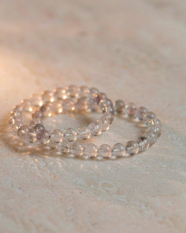 Two clear quartz bead bracelets resting on a sunlit stone surface in warm light