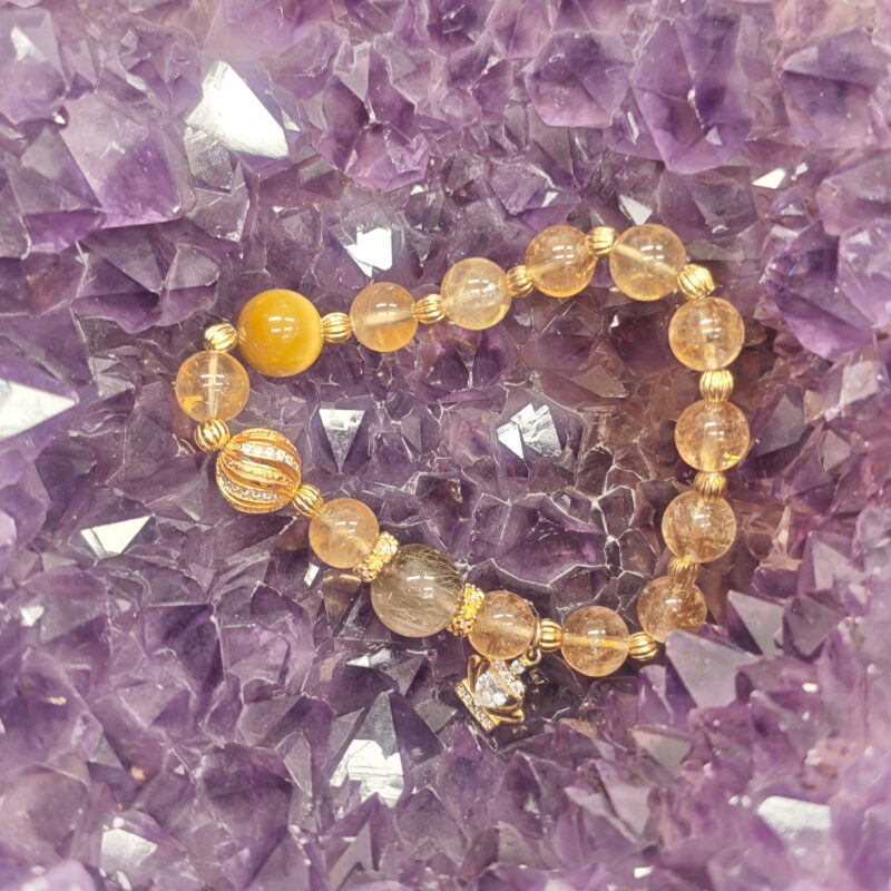 Golden rutilated quartz and citrine bracelet resting on a cluster of clear and purple crystals.