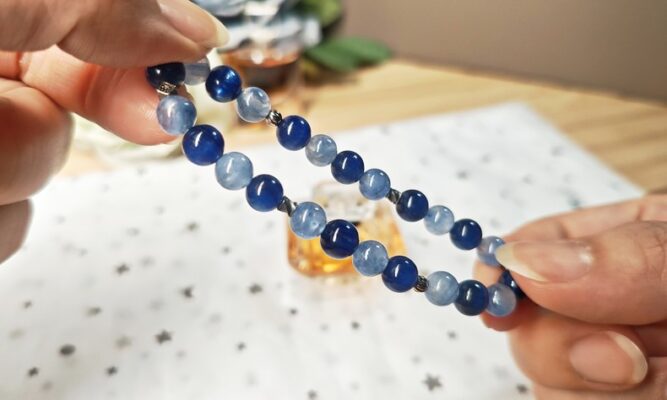 Hands holding a two-tone blue kyanite bracelet above a star-print cloth.