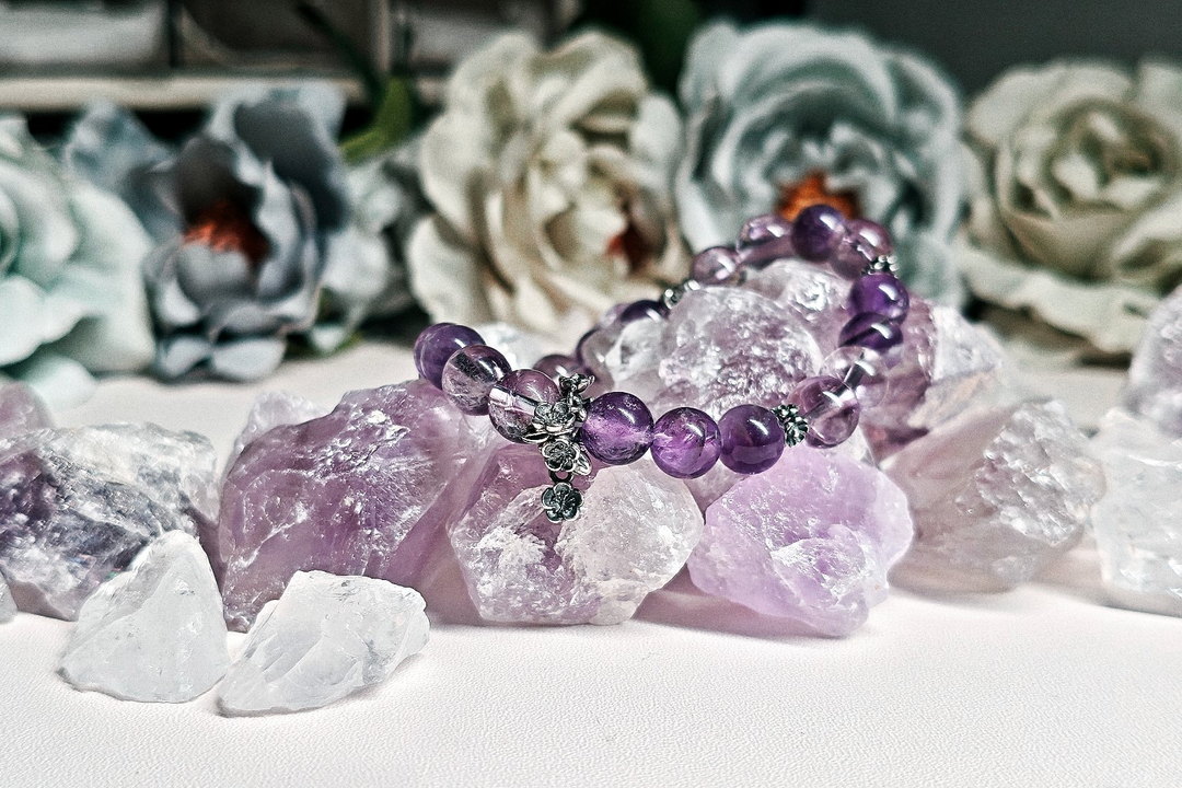 Amethyst crystal bracelet resting on raw amethyst and quartz, with dried flowers behind