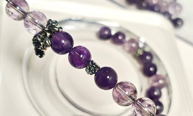 Amethyst crystal beads strung with silver spacers on a white tray, with loose amethyst beads scattered around.