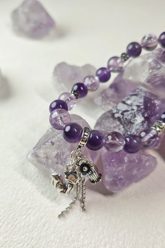 Close-up of deep purple amethyst and ice lavender quartz beads with a silver fox charm and chain tassel.