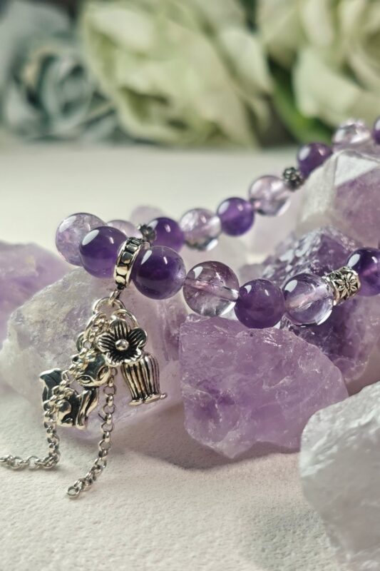 Amethyst and ice lavender quartz bracelet resting on raw amethyst stones, with a small silver fox charm.