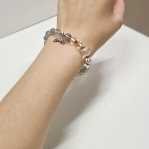 Woman wearing the Gray Moonstone Tide Bracelet with clear quartz and sterling silver mermaid tail charm as an everyday symbol of calm and protection