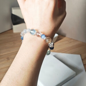 Woman wearing the Veil Crystal Bracelet AuroraGain CL with layered gold, blue, and clear natural crystals