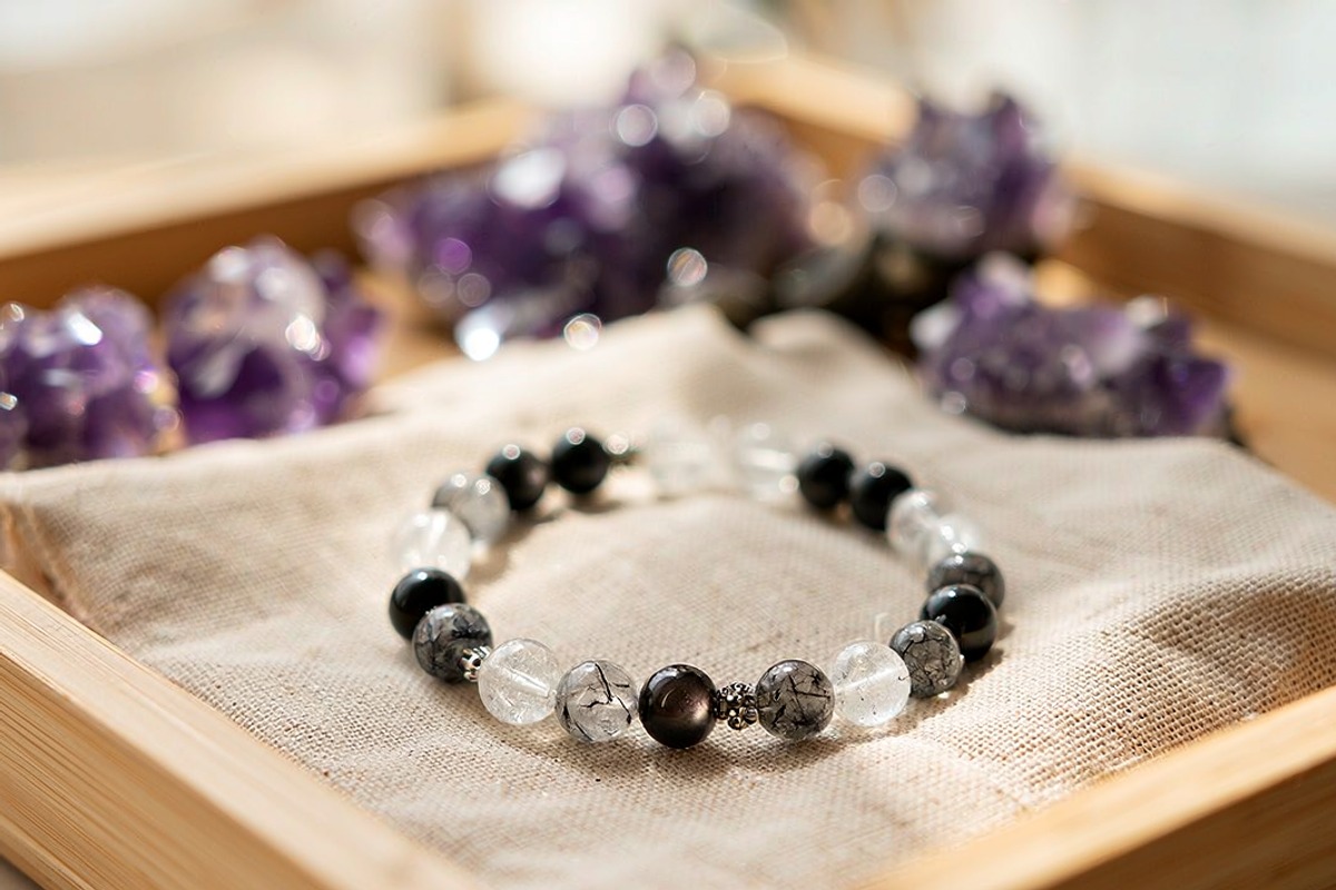 Black obsidian and crackle quartz crystal bracelet on linen cloth in wooden tray with amethyst bokeh background