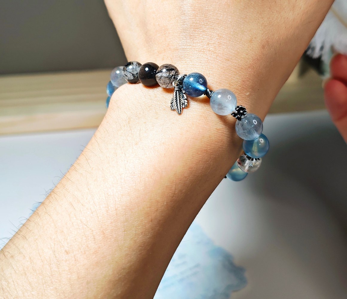 Aquamarine bracelet with rutilated quartz and silver feather charm worn on the wrist