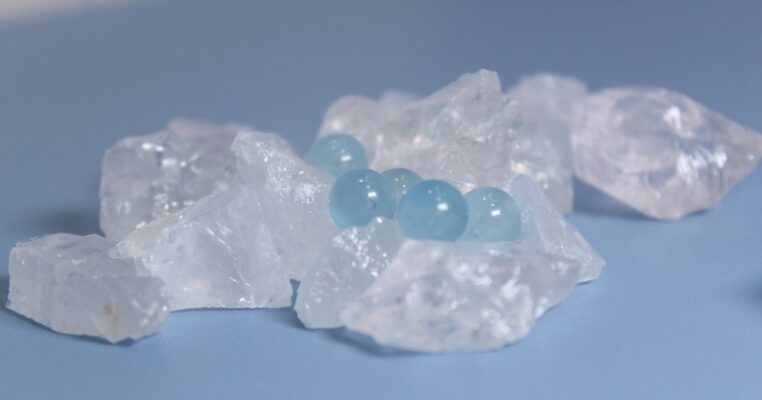 Aquamarine beads nestled among raw clear quartz crystals on a blue background