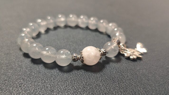 Blue rutilated quartz bead bracelet with a silver butterfly charm, close-up on a grey fabric background