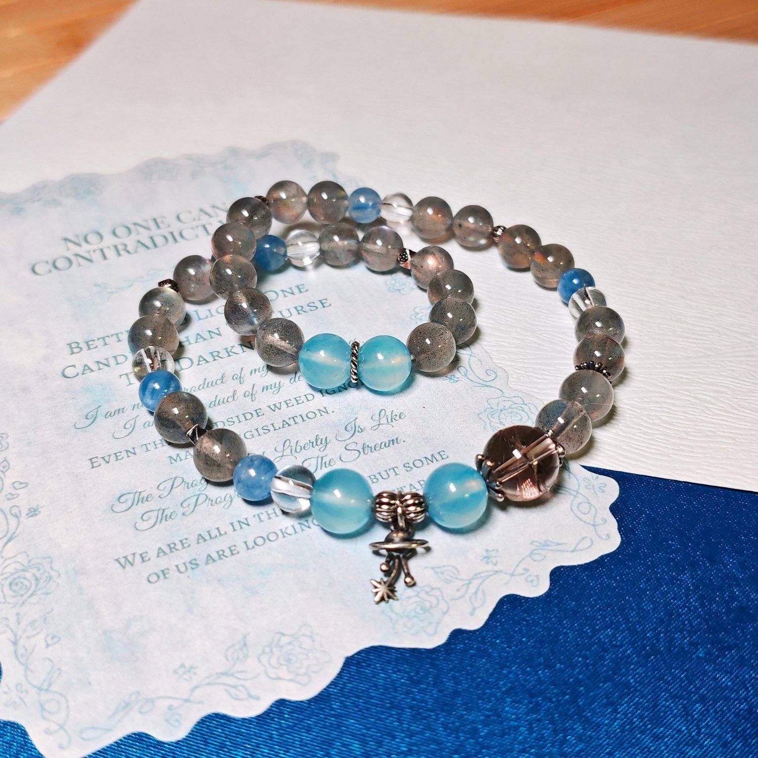 The Career Orbit crystal bracelet laid flat on a printed page, with blue aquamarine beads and a small silver planet charm at the centre.