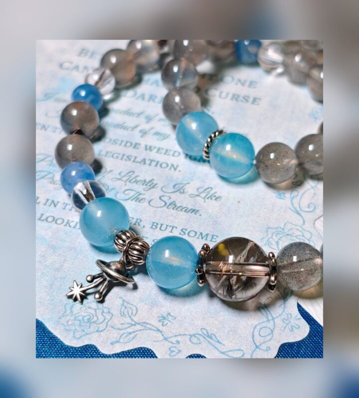 The Career Orbit crystal bracelet arranged as a full circle on a vintage printed page, with aquamarine and kyanite beads and a small silver planet charm.