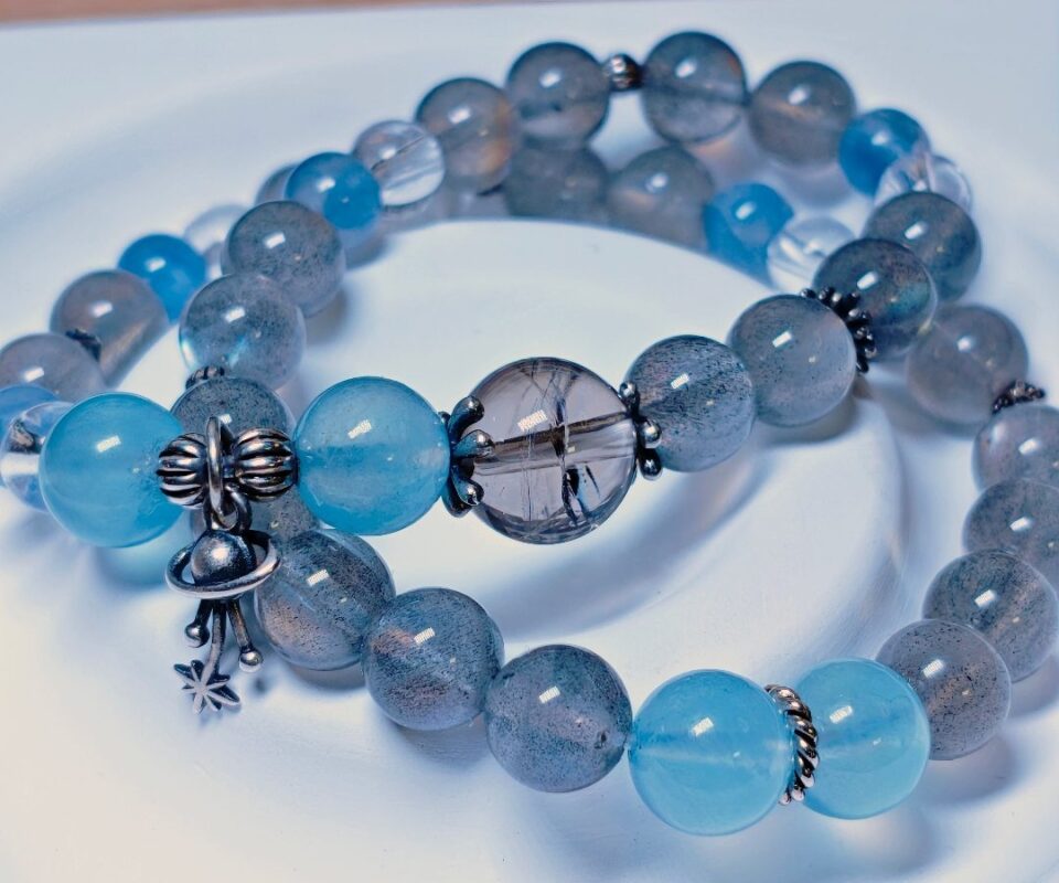 The Career Orbit crystal bracelet in a full circle on a white plate, with aquamarine, kyanite, moonstone and black-gold quartz beads.