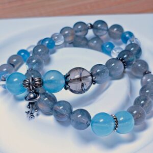 The Career Orbit crystal bracelet arranged as a full circle on a pale plate, with aquamarine, kyanite, moonstone, black-gold quartz and clear quartz beads.