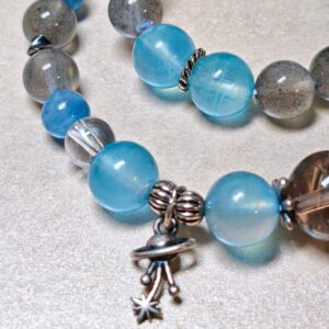 A close-up of the Career Orbit crystal bracelet, showing its blue aquamarine beads, speckled black-gold quartz, and a small silver planet charm.