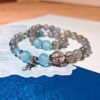 The Career Orbit crystal bracelet coiled on a printed page, with blue aquamarine and kyanite beads, dark black-gold quartz beads, and a small silver planet charm.