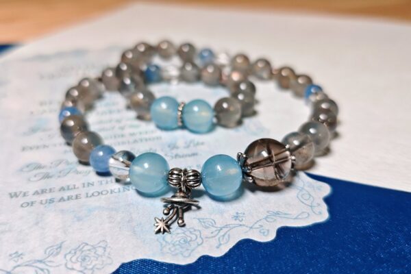 A crystal bracelet for women styled on printed paper and blue linen, showing bead size and a silver charm