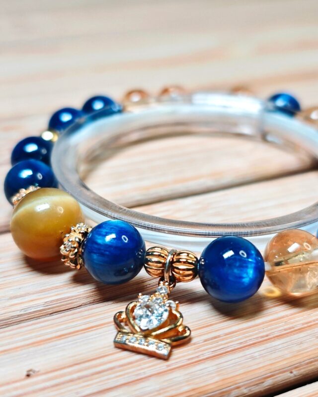 Bracelet on a pale wood surface with the gold-tone crown charm hanging at the front of the strand