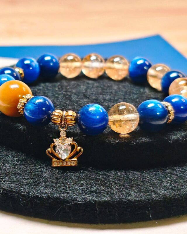 Bracelet on a black felt display, gold crown charm hanging at the centre of the strand