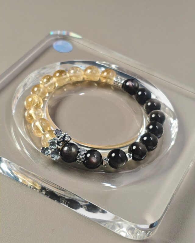 Full view of the equinox crystal bracelet, half silver obsidian and half ice citrine, resting on a clear tray