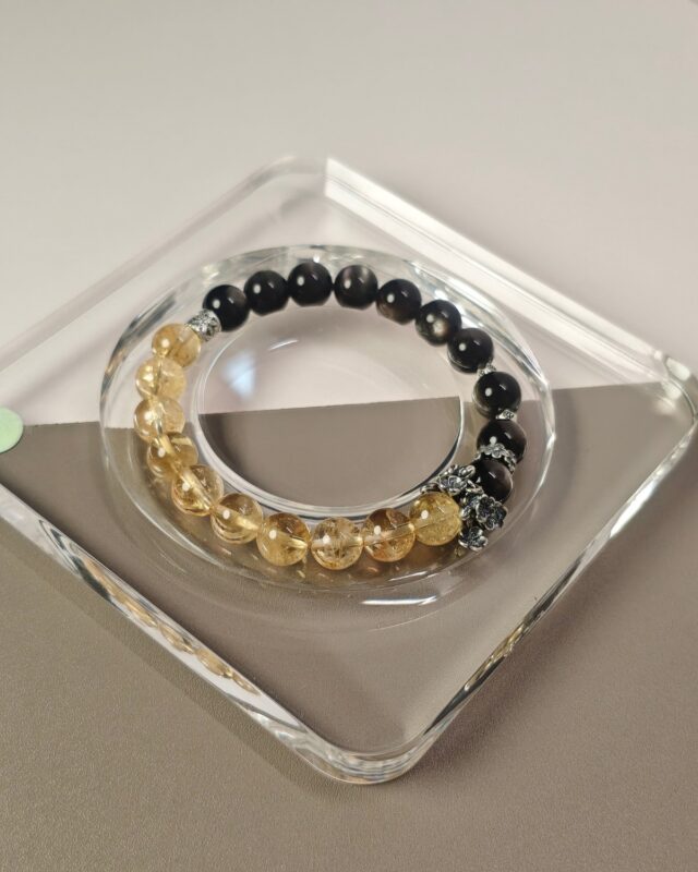 Two-tone silver obsidian citrine bracelet on a clear tray, black beads on one side and pale gold on the other