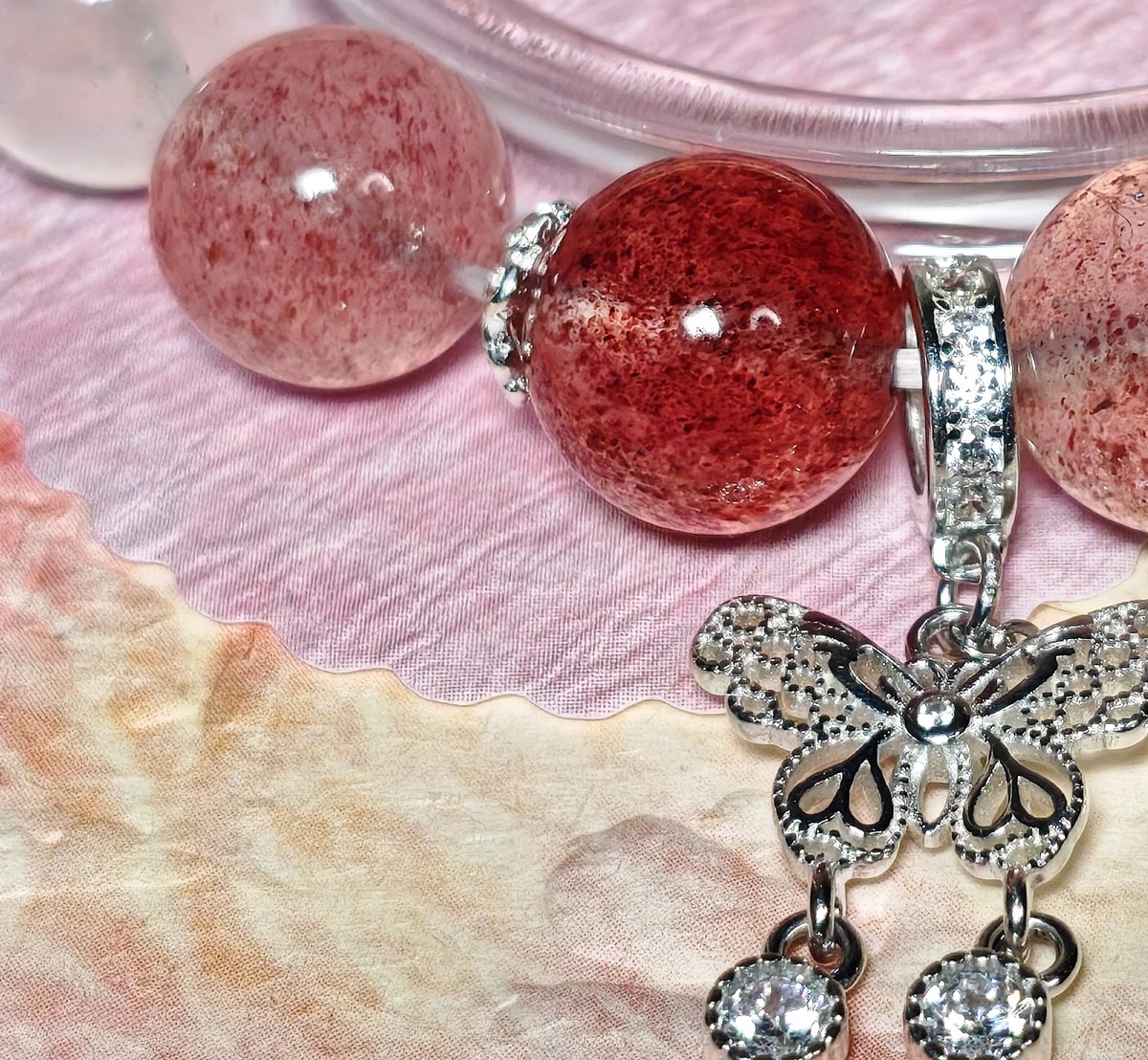 Close-up of speckled strawberry quartz and clear quartz beads with a sterling silver butterfly charm