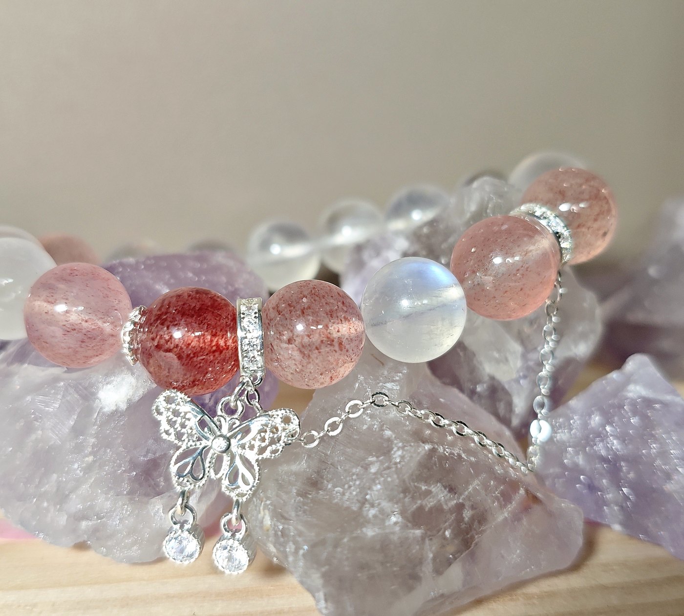 Eternal Metamorphosis crystal bracelet with strawberry quartz beads and butterfly charm resting on raw crystals