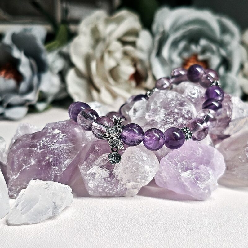 Evening Stillness amethyst crystal bracelet resting on raw amethyst stones among pale roses.