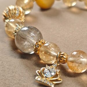Angled display of the golden rutilated quartz and citrine bracelet, showing the bead sequence and the gold crown charm.