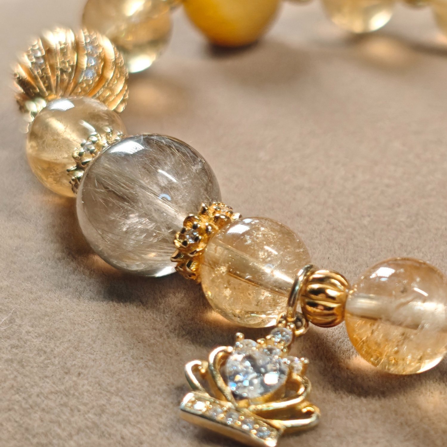 Angled display of the golden rutilated quartz and citrine bracelet, showing the bead sequence and the gold crown charm.