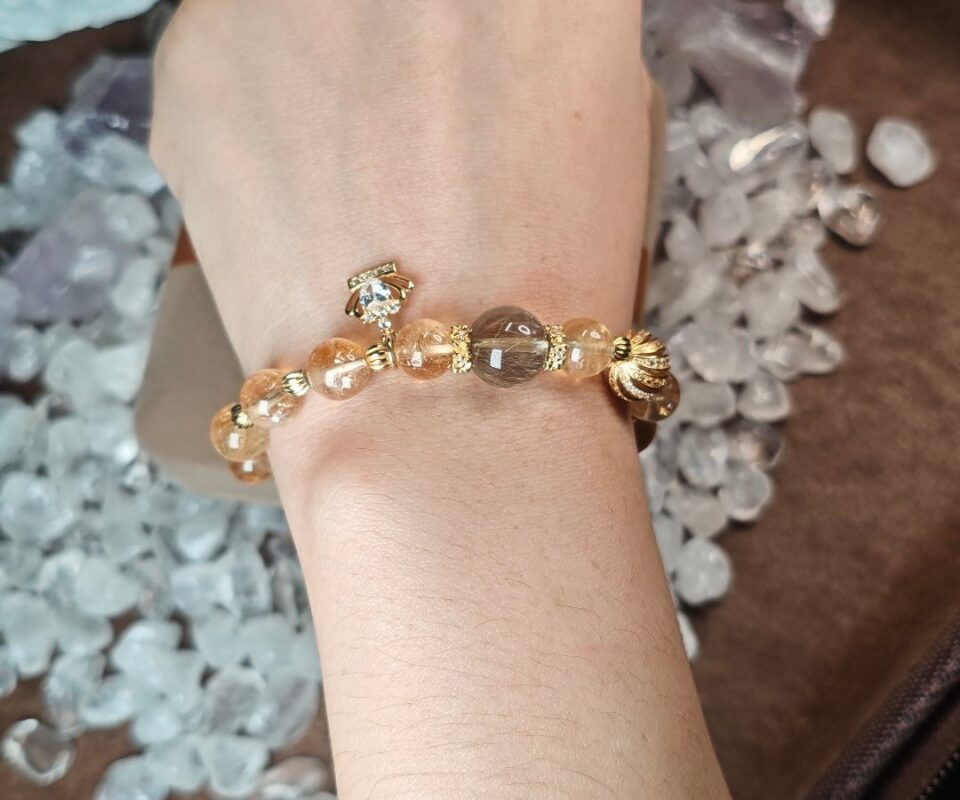 Golden rutilated quartz and citrine bracelet worn on the wrist, with the gold crown charm and clear quartz crystals around it.