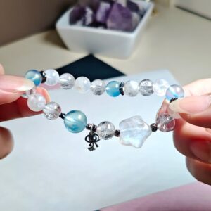 Bracelet held up between two fingers, aquamarine and ice clear quartz beads with the planet charm below