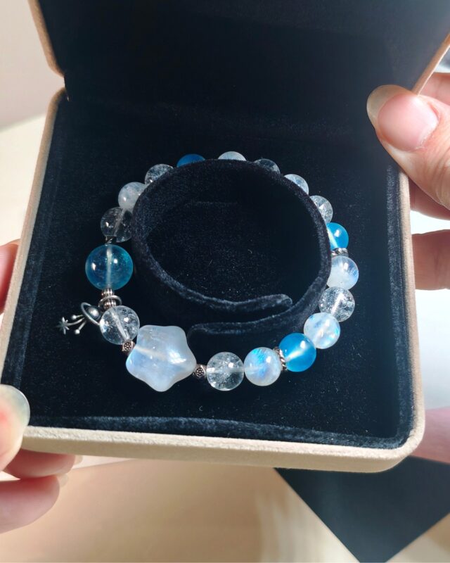 Bracelet resting inside its gift box, pale blue beads and s925 sterling silver charm against the dark lining