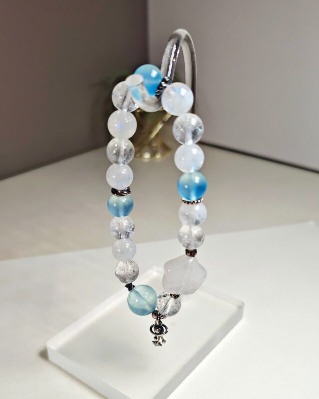 Blue moonstone aquamarine clear quartz bracelet hung on a clear display stand, s925 sterling silver planet charm at the bottom