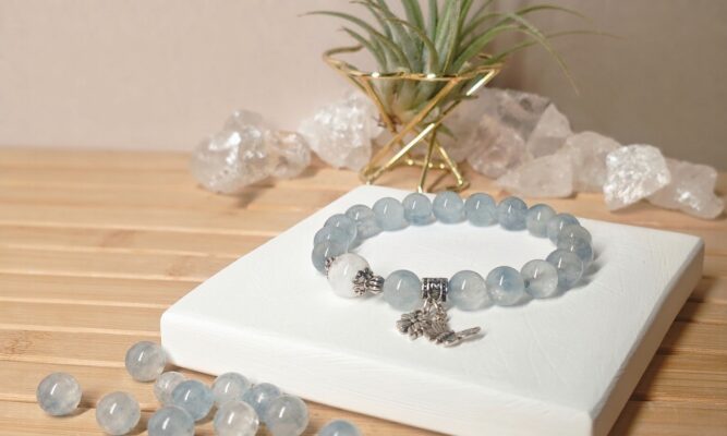 Phantom quartz meaning illustrated by a beaded bracelet with white phantom and pale blue rutilated quartz beads on a white display block