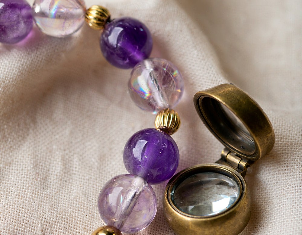 Macro view of genuine amethyst and lavender quartz beads beside an open brass loupe, showing the natural inclusions real beads carry.