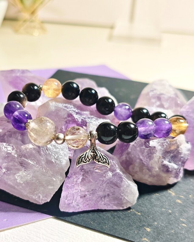 Rising Current crystal bracelet resting among raw amethyst pieces on a dark slate tray.