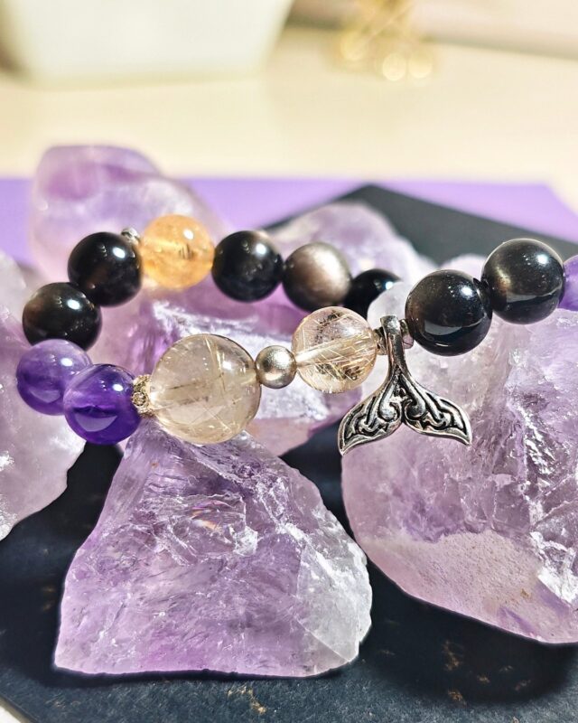Rising Current crystal bracelet draped over raw amethyst pieces, showing its black obsidian, amethyst, Ice Citrine and golden rutilated quartz beads.