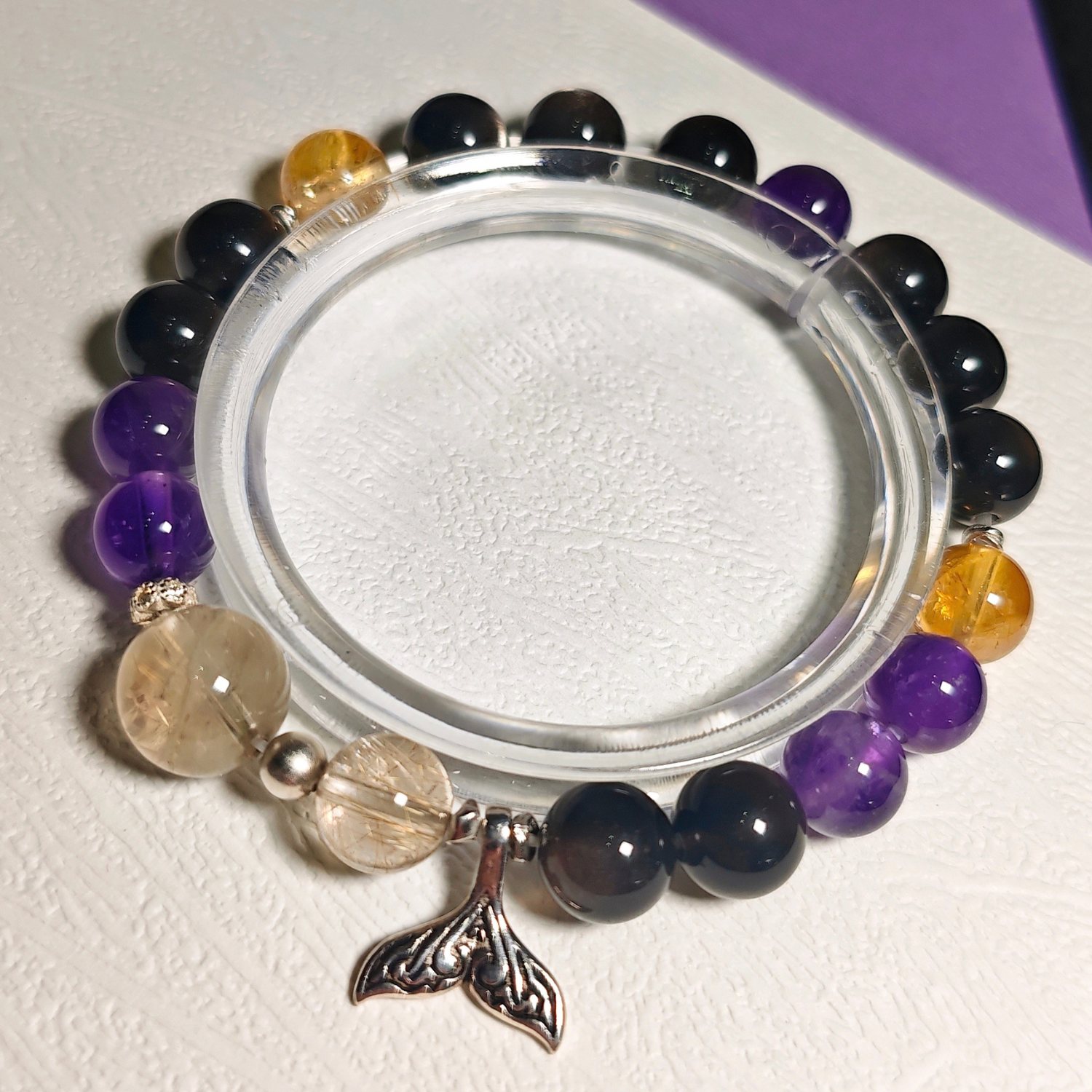 Rising Current crystal bracelet shown full circle on a clear stand, with its S925 sterling silver mermaid tail charm at the front.