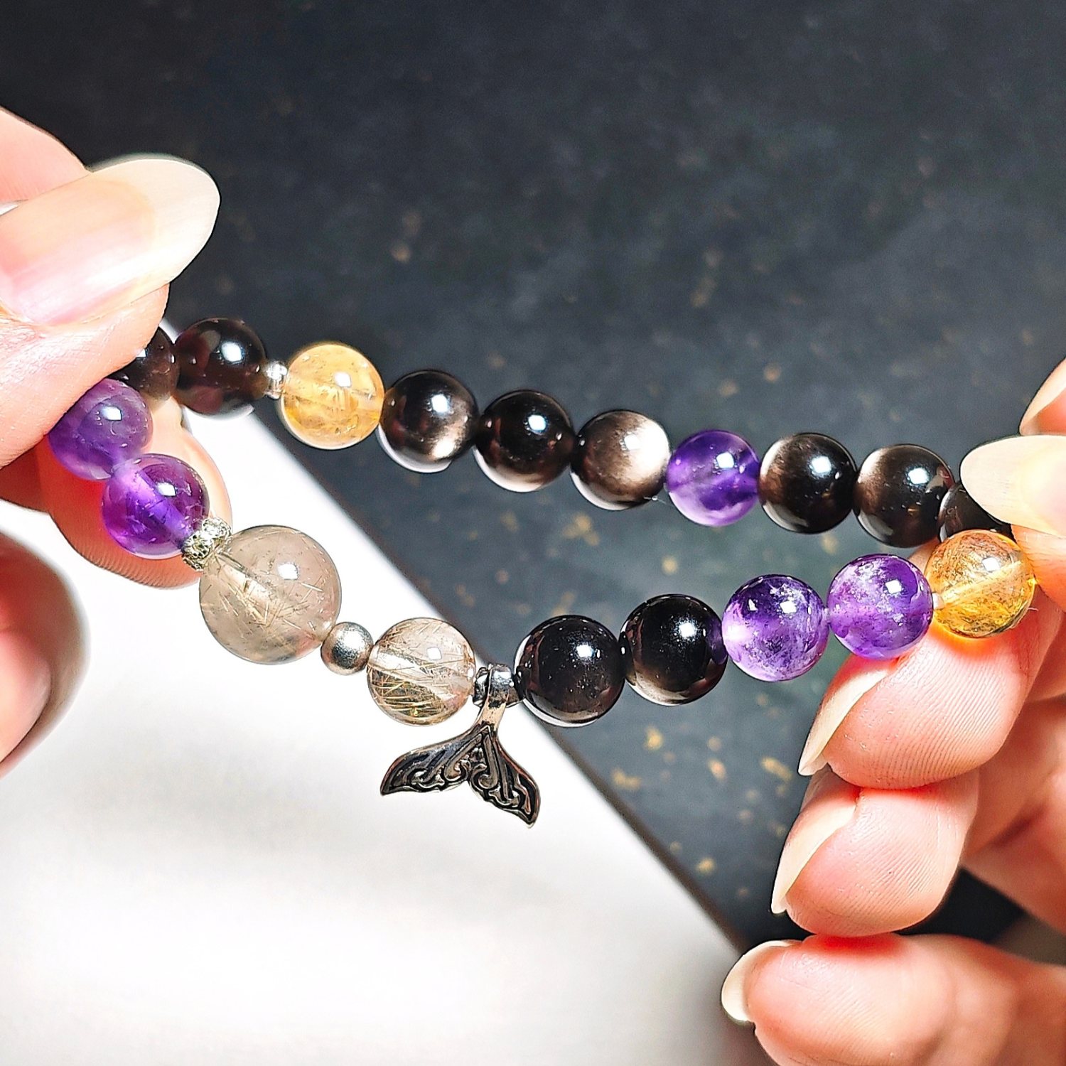 Mermaid tail crystal bracelet held in two hands, showing the order of the black, gold and purple beads.