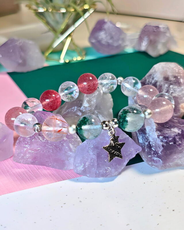 Rooted Glow crystal bracelet resting against raw amethyst pieces, with its star charm in view.