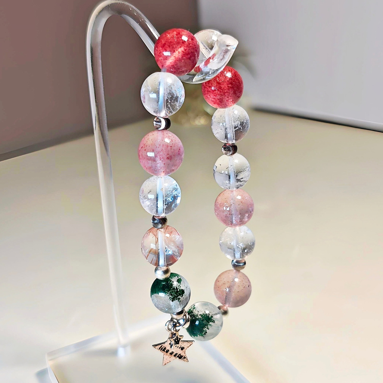 Black gold super seven bracelet hanging on a stand, showing the order of the green, pink and bronze beads.