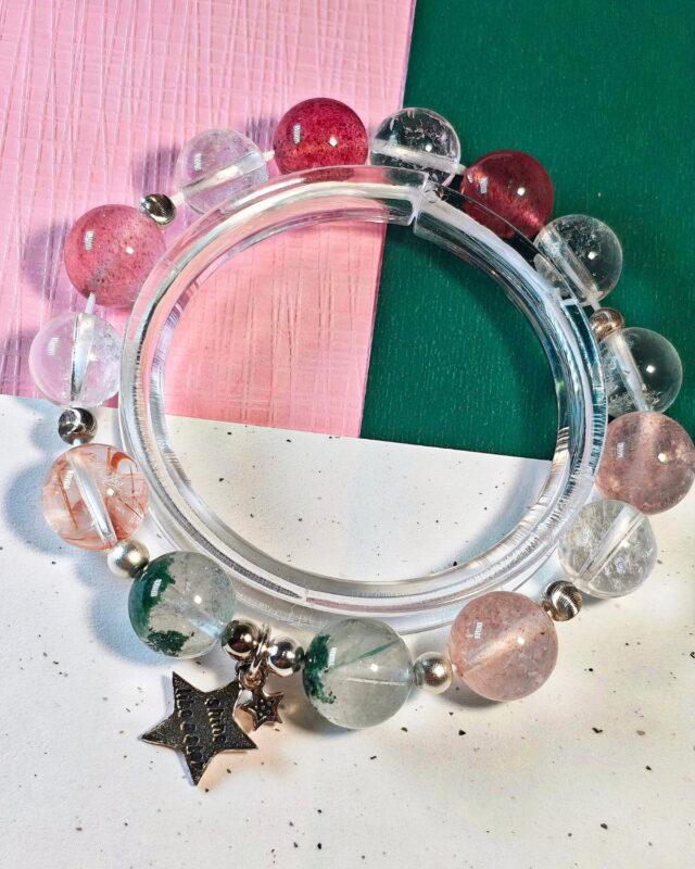 Rooted Glow crystal bracelet resting on a clear stand over soft pink and green cloth.
