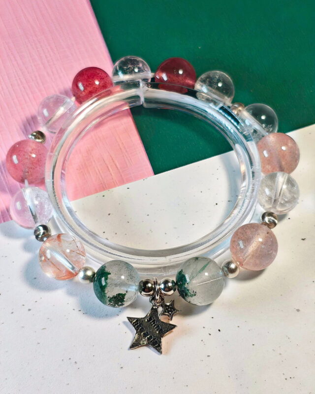 Rooted Glow crystal bracelet on a clear display stand over a pink and green cloth, with its sterling silver star charm at the front.