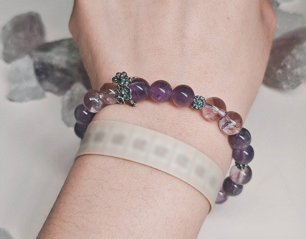 Woman's wrist with an amethyst crystal bracelet and a soft measuring tape wrapped below it, showing how to measure for the right fit