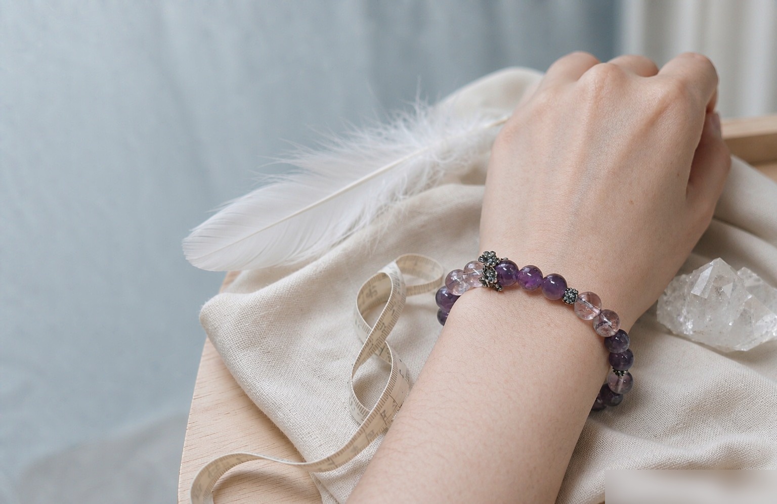 Amethyst and ice lavender quartz bracelet worn on a wrist beside a soft measuring tape on ivory linen