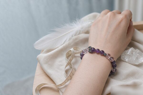 Crystal bracelet size guide: an amethyst and ice lavender quartz bracelet worn on a wrist with a soft measuring tape on ivory linen