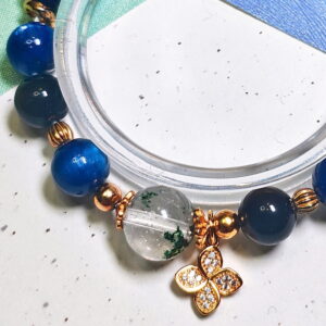 Close view of the green phantom quartz bracelet, showing its deep blue kyanite beads and four-leaf clover charm.